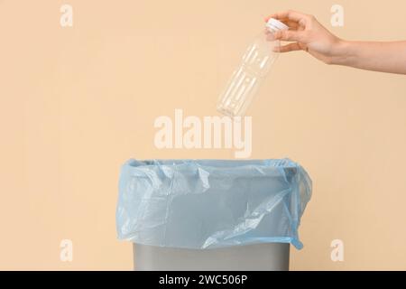 Donna che lancia una bottiglia di plastica vuota nel cestino vicino alla parete beige, primo piano Foto Stock