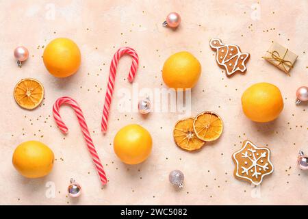 Gustose arance con canne di caramelle, biscotti dolci e palline di Natale su sfondo beige Foto Stock