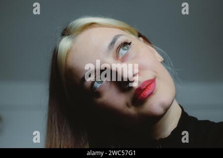 Una donna splendida con capelli fluenti e lussureggianti e accattivanti occhi blu guarda tranquillamente in lontananza Foto Stock