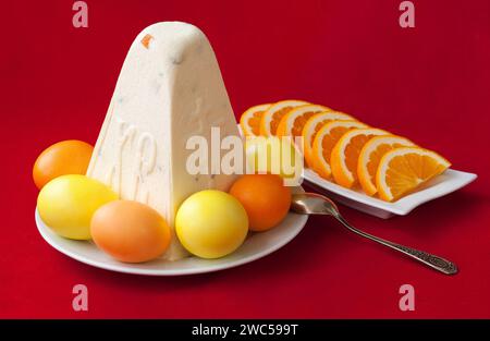 Dolce tradizionale paskha con formaggio pasquale con uova e arance su fondo rosso. Sfondo pasquale moderno e minimalista con spazio per la copia Foto Stock