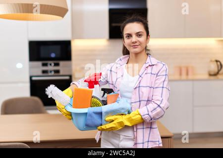 Donna in guanti protettivi di gomma gialli che tiene il secchio con detergenti e stracci per la pulizia . faccende domestiche. Foto Stock