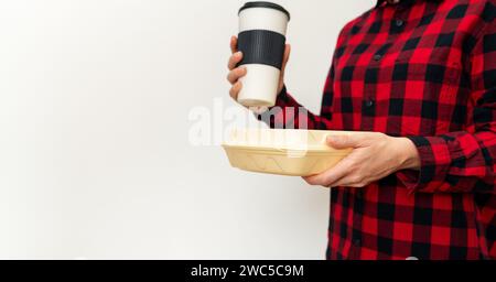 Pranzo al sacco e tazza da caffè in mani femminili su sfondo semplice con spazio per le copie. Foto Stock