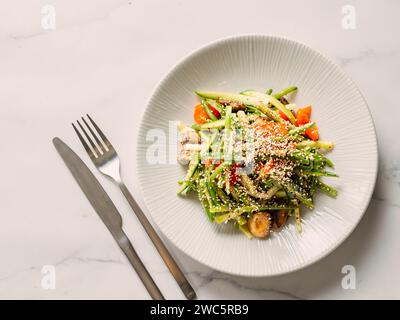 Deliziosa insalata di carne di maiale con cetriolo in stile asiatico con popcorn all'amaranto o amaranto (sesamo sostituibile) su fondo di marmo bianco. Topvi Foto Stock