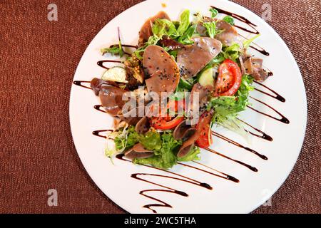 Insalata con lingua di manzo con verdure ed erbe aromatiche, condite con la salsa su una piastra bianca. Foto Stock