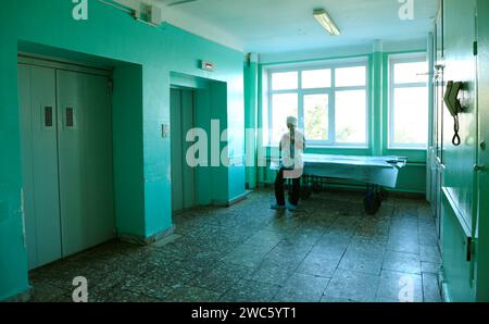 Medico donna in un camice blu in piedi nel corridoio dell'ospedale, in attesa di un ascensore, barella. Kiev, Ucraina Foto Stock