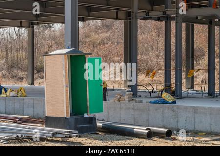 Chungju, Corea del Sud, 22 marzo 2020: Solo per uso editoriale. Port-a-Potty con porta aperta nel cantiere vicino a un edificio industriale incompiuto Foto Stock