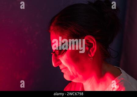 Primo piano sulla faccia di una donna anziana che esegue la sessione di terapia a luce rossa con pannello e protezione per gli occhi Foto Stock