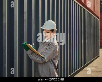 Ingegnere donna asiatica che lavora nel terminal del porto container. elaborare gli ordini e i prodotti presso il magazzino logistico per il carico per l'importazione e l'esportazione Foto Stock