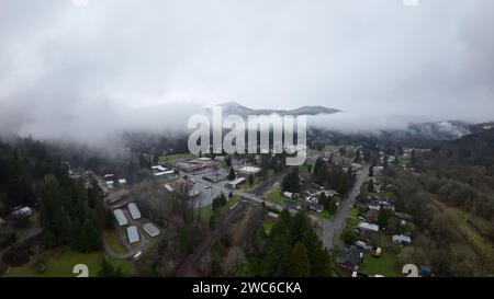 Una vista incantevole di una pittoresca cittadina annidata tra maestose montagne, mentre la nebbia eterea scende delicatamente dalle cime Foto Stock