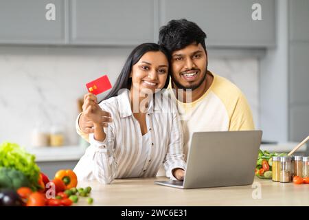 Sorridente coppia orientale con portatile, acquisto con carta di credito in cucina Foto Stock