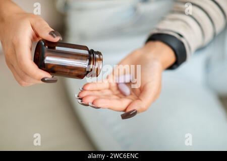 Immagine mirata di una donna a casa che le versa pillole viola in mano da una bottiglia di medicina marrone Foto Stock
