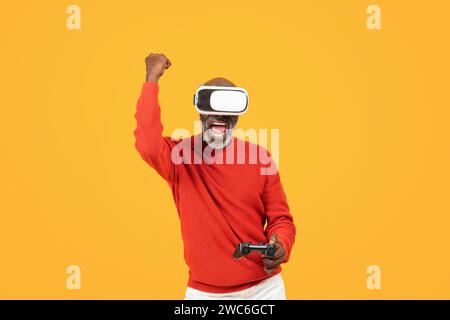 Felice vincitore senior afroamericano con controller di gioco in mano e occhiali vr Foto Stock