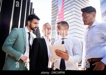 Gruppi di uomini d'affari si sono riuniti fuori da uffici che si guardano a vicenda consulenze seri su tablet. Foto Stock