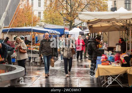 La gente attraversa il mercato in una giornata di pioggia nella piazza del teatro di Anversa. Foto Stock