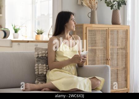 Una giovane donna sorridente tiene il telefono cellulare guardando lontano Foto Stock