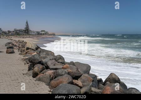 Paesaggio urbano con onde dell'oceano Atlantico sulla spiaggia sabbiosa della città storica, su dune gialle sullo sfondo, scattate in tarda primavera a Swakopomund, er Foto Stock