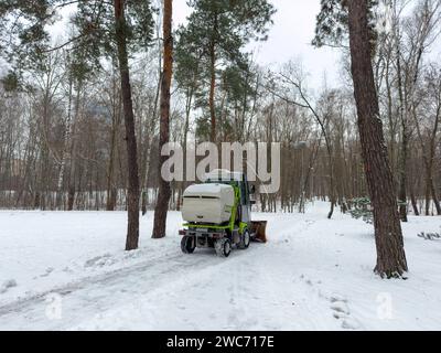 I lavoratori municipali puliscono un parco cittadino su un trattore. Il servizio cittadino pulisce la neve , un piccolo e grazioso trattore con una spazzola rotante pulisce una strada in città Foto Stock