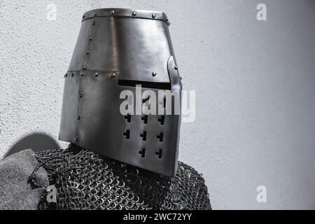 Armatura in acciaio di un cavaliere crociato medievale. Casco in ferro chiuso e catena su parete grigia Foto Stock