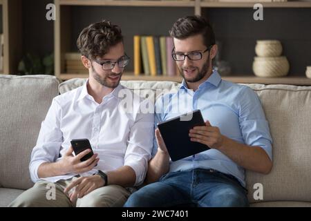 Due fratelli gemelli seduti sul divano con i dispositivi Foto Stock