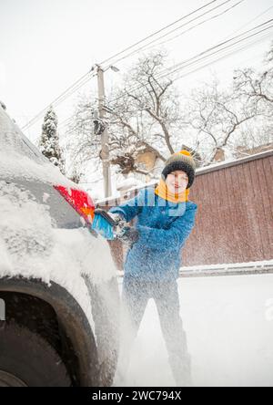 Il bambino carino sta aiutando suo padre a spazzolare la neve dalla macchina. Rimozione della neve dalla vettura - il concetto di cura della vettura durante l'inverno. Foto Stock