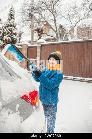 Il bambino carino sta aiutando suo padre a spazzolare la neve dalla macchina. Rimozione della neve dalla vettura - il concetto di cura della vettura durante l'inverno. Foto Stock