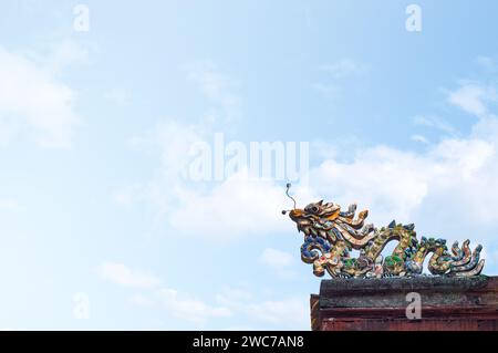 Una tradizionale scultura di drago, dettagliatamente dettagliata, si trova in cima a un'antica casa vietnamita, a simboleggiare potere e prosperità sotto un blu chiaro Foto Stock