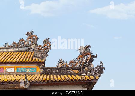 Una tradizionale scultura di drago, dettagliatamente dettagliata, si trova in cima a un'antica casa vietnamita, a simboleggiare potere e prosperità sotto un blu chiaro Foto Stock