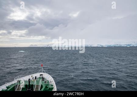 Shiip entra nella baia di Brialmont< antartide in una giornata nuvolosa in primavera, IIce e costa innevata con archi di ghiaccio e grotte Foto Stock