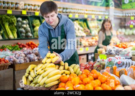 Un giovane venditore che mette le banane in un cestino del mercato in un grande negozio di alimentari Foto Stock