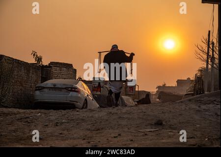 Nuova Delhi, India. 14 gennaio 2024. Un rifugiato Rohingya torna a casa portando acqua potabile su un palo prelevato da un punto di distribuzione nel campo profughi di Madanpur Khadar Rohingya. 1.100 Rohingya che vivono nei campi di Madanpur Khadar dipendono dall'approvvigionamento idrico comunale. (Immagine di credito: © Pradeep Gaur/SOPA Images via ZUMA Press Wire) SOLO PER USO EDITORIALE! Non per USO commerciale! Foto Stock