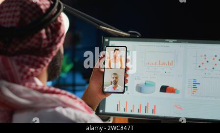 Telelavoratore islamico e colleghi nel controllo delle videochiamate su Internet insieme di dati statistici. Dipendenti arabi che ottimizzano gli indicatori chiave delle prestazioni nelle riunioni di teleconferenza, primo piano Foto Stock