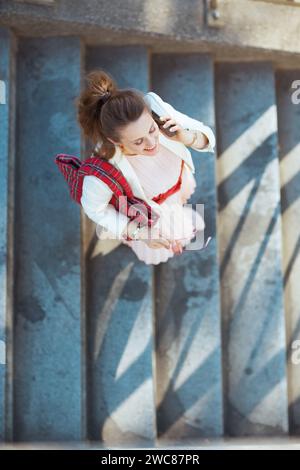 Vista dall'alto di una donna sorridente di mezza età in abito rosa e giacca bianca della città con borsa rossa che parla su uno smartphone. Foto Stock