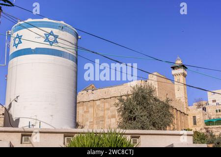 La torre dell'acqua con la bandiera israeliana di fronte alla Tomba dei Patriarchi nel centro della città palestinese di Hebron, Cisgiordania, Palestina. Foto Stock