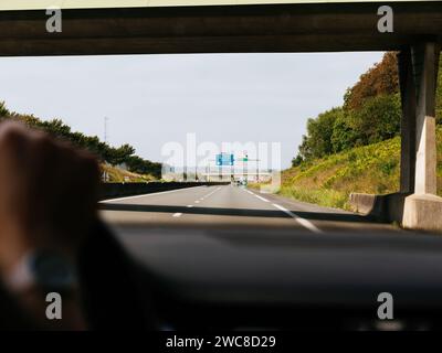 Catturata dal punto di vista del conducente, questa immagine mostra una giornata limpida sull'autostrada mentre passiamo sotto un cavalcavia di cemento, con il viaggio che si estende avanti, guidando verso le Touquetm Boulogne, Calais in Francia, e anche a Berck Foto Stock