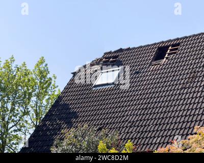 Vista del tetto di una casa danneggiata con fori visibili e piastrelle mancanti, che indica la necessità di riparazioni urgenti. Foto Stock