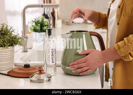 Donna che aggiunge bicarbonato di sodio nel bollitore elettrico in cucina, primo piano Foto Stock