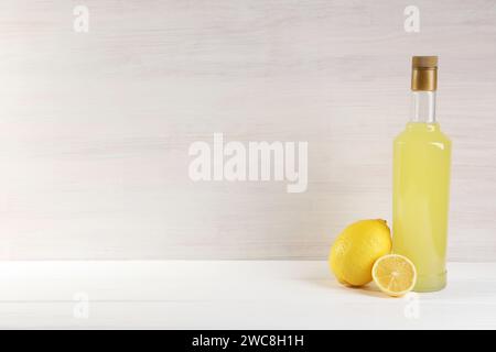 Bottiglia di saporito liquore al limoncello e limoni su tavolo in legno bianco, spazio per testo Foto Stock