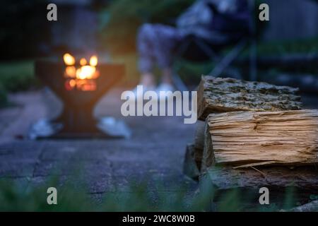 Tronchi di legno tagliati. Fuoco da campeggio, fossa piena di legna bruciata e fiamme. Un camper seduto sullo sfondo. Foto Stock