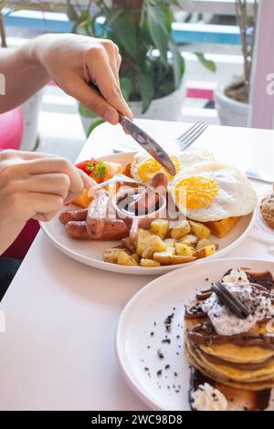 Colazione all'americana con uova fritte patate saltate salsicce e frutta. Servita nel ristorante. Foto Stock