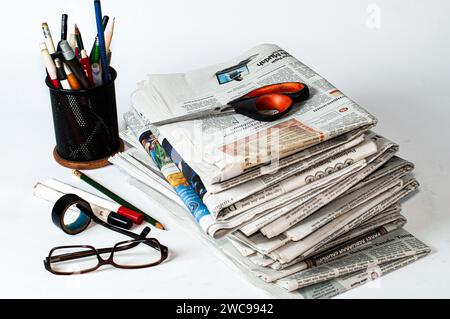 pile di giornali che devono essere letti per ottenere informazioni sulle notizie aziendali e finanziarie, oltre a cancelleria e bicchieri sul tavolo Foto Stock