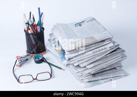 pile di giornali che devono essere letti per ottenere informazioni sulle notizie aziendali e finanziarie, oltre a cancelleria e bicchieri sul tavolo Foto Stock