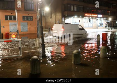 Amburgo, Germania. 15 gennaio 2024. L'acqua dell'Elba viene spinta sul Große Elbstraße al mercato del pesce di Amburgo durante un'ondata di tempesta. Un'auto passa attraverso l'acqua. Lunedì mattina, l'ondata di tempesta ha spinto ancora una volta molta acqua a riva sulla costa del Mare del Nord e nei fiumi Elba e Weser. Ad Amburgo, il mercato del pesce e il Große Elbstraße erano completamente sott'acqua. Secondo la Federal Maritime and Hydrographic Agency (BSH), l'acqua al St. La sagoma di Pauli era salita a circa 2,30 metri sopra l'acqua media poco prima delle 7,00 del mattino. Credito: Bodo Marks/dpa/Alamy Live News Foto Stock