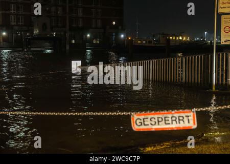 Amburgo, Germania. 15 gennaio 2024. L'acqua dell'Elba ha inondato un parcheggio chiuso ad Amburgo-Övelgönne durante un'ondata di tempesta. Lunedì mattina, l'ondata di tempesta ha spinto ancora una volta molta acqua a riva sulla costa del Mare del Nord e nei fiumi Elba e Weser. Ad Amburgo, il mercato del pesce e il Große Elbstraße erano completamente sott'acqua. Secondo la Federal Maritime and Hydrographic Agency (BSH), l'acqua al St. La sagoma di Pauli era salita a circa 2,30 metri sopra l'acqua media poco prima delle 7,00 del mattino. Credito: Bodo Marks/dpa/Alamy Live News Foto Stock