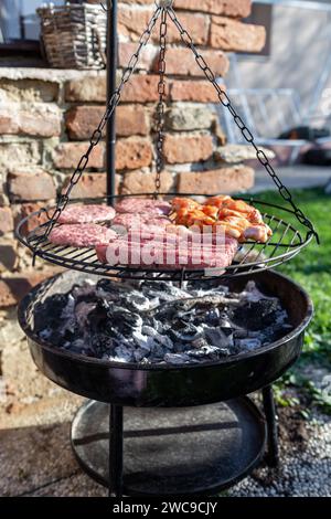 Grigliare con carne cruda. Ci sono cevapcici e hamburger per grigliare. Era estate e l'ora del barbecue. Il cibo viene cucinato su carbone caldo in Foto Stock