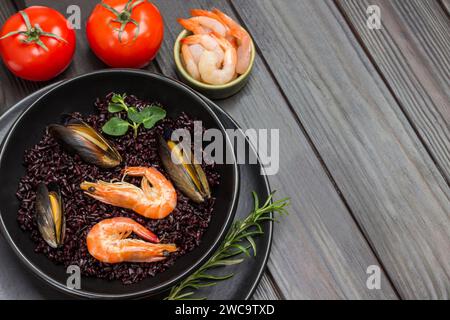 Gamberi e cozze con riso nero sul piatto. Pomodori e gamberi nel recipiente. Sfondo di legno scuro. Copia spazio. Vista dall'alto Foto Stock