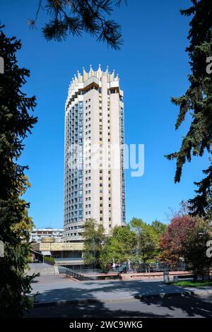 Una vista attraverso gli alberi dell'iconico Hotel Kazakhstan, a 26 piani, aperto nel 1977. È un esempio di architettura socialista sovietica, modernista. In al Foto Stock