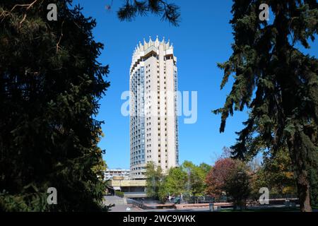 Una vista attraverso gli alberi dell'iconico Hotel Kazakhstan, a 26 piani, aperto nel 1977. È un esempio di architettura socialista sovietica, modernista. In al Foto Stock