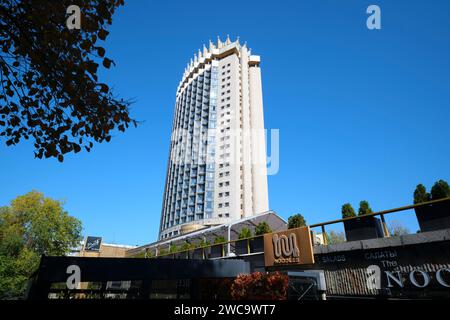 Una vista attraverso gli alberi dell'iconico Hotel Kazakhstan, a 26 piani, aperto nel 1977. È un esempio di architettura socialista sovietica, modernista. In al Foto Stock