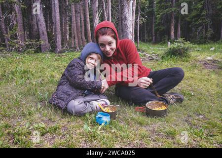 Madre e bambino che si godono il pasto in campeggio nella foresta Foto Stock