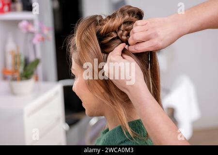 Vista laterale del parrucchiere femminile anonimo che fa parrucchiere al cliente in un salone di bellezza professionale Foto Stock